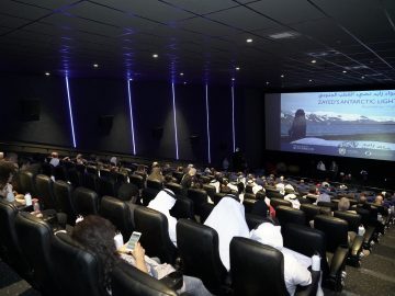 People sitting in a theatre and watching a movie on screen