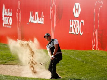 Golfer getting the ball out of sand pit with a swing sending the sand fly in the air