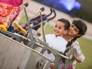 A young boy in white shirt and a girl in floral dress smilingly paying with a rotating maching