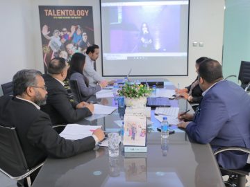 Group of people sitting around a table and looking at a projection on a screen