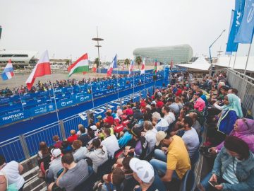 Back of people sitting in a stadium style sitting with different country flags in the foreground