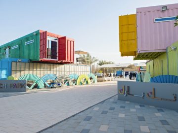 Ship cargo containers painted in red, green, yellow and pink stacked on each other with a cut open door on them