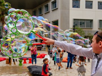 Hand shot of a bubble maker making bubbles with kids looking at the bubbles in the background